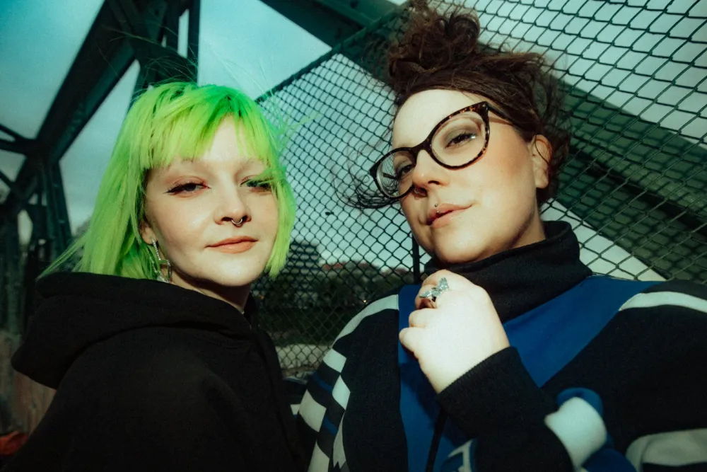 Das Wiener DJ-Duo DIAL 1808, Steffi und Viki, vor einem Maschendrahtzaun