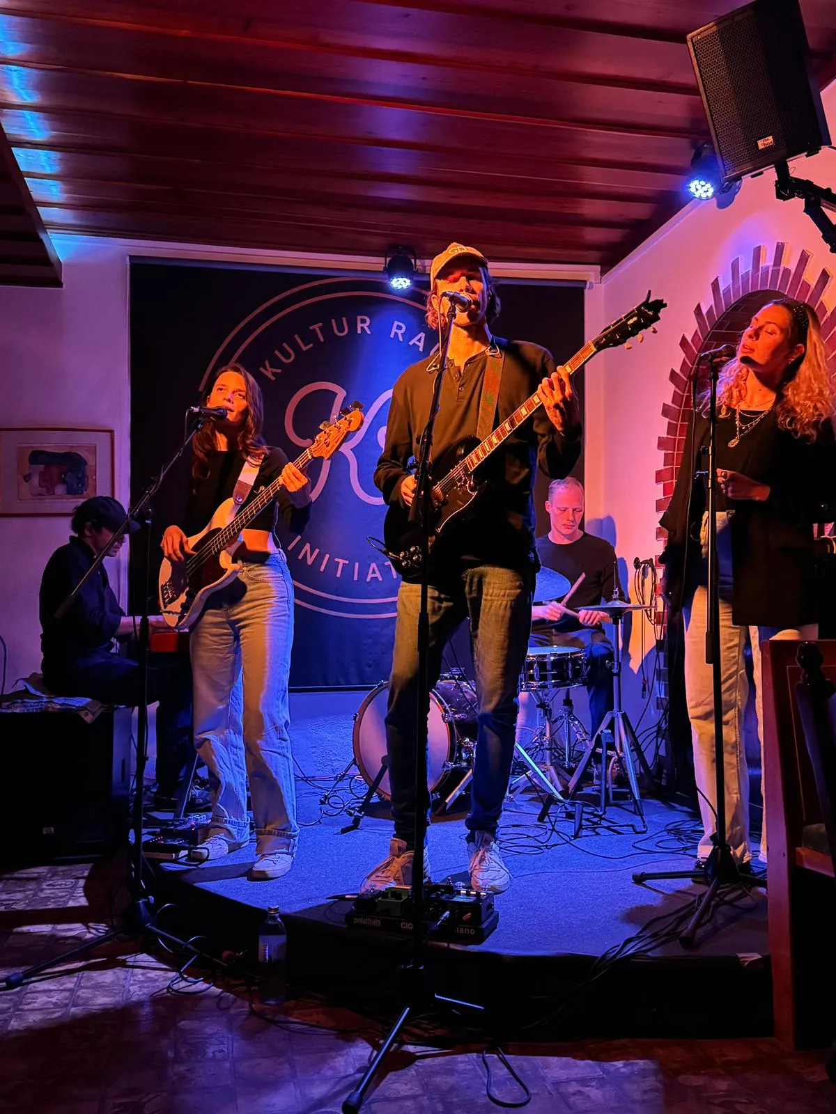 Gabriel Denk mit Band auf der KRI-Bühne bei blauem Licht, zwei Sängerinnen an den Mikrofonen