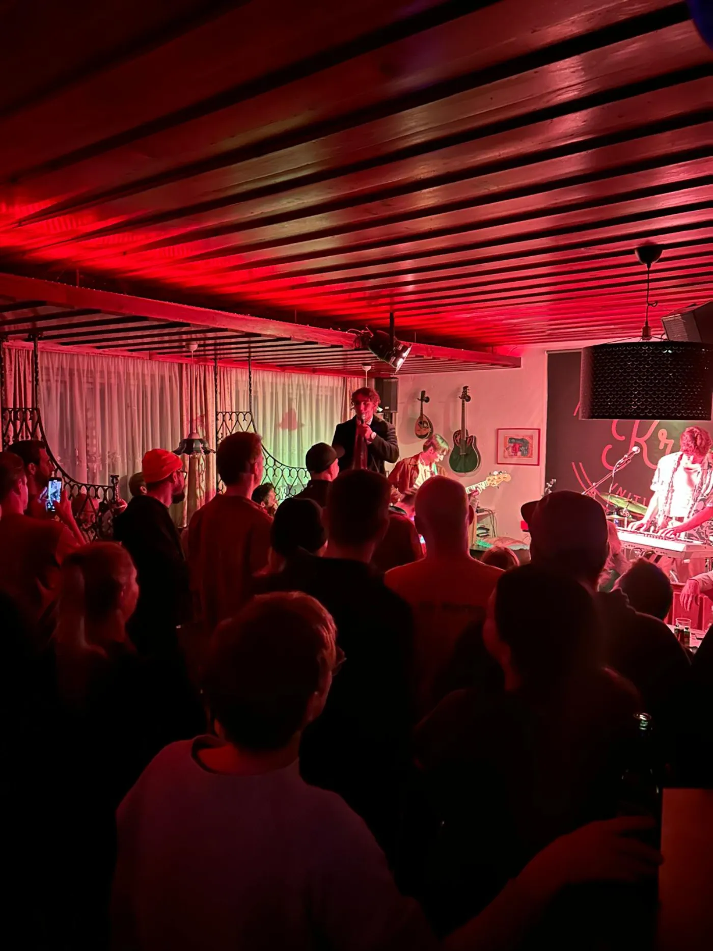 Voller Raum im KRI bei rotem Licht: Publikum dicht vor der Bühne, im Hintergrund die Band